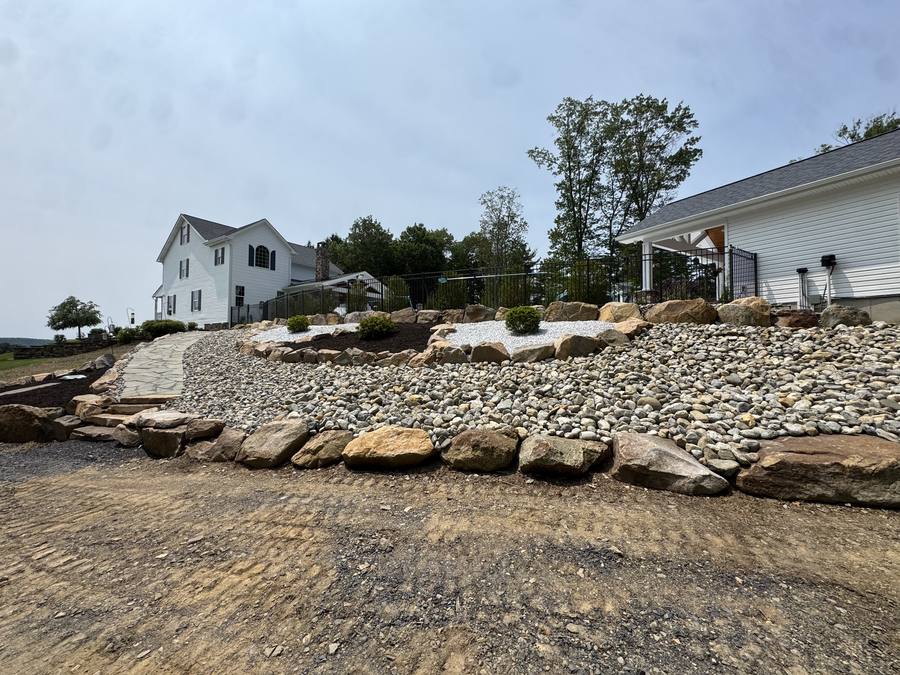 Terraced river rock and boulder landscape bed with flagstone walkway leading to a farmhouse