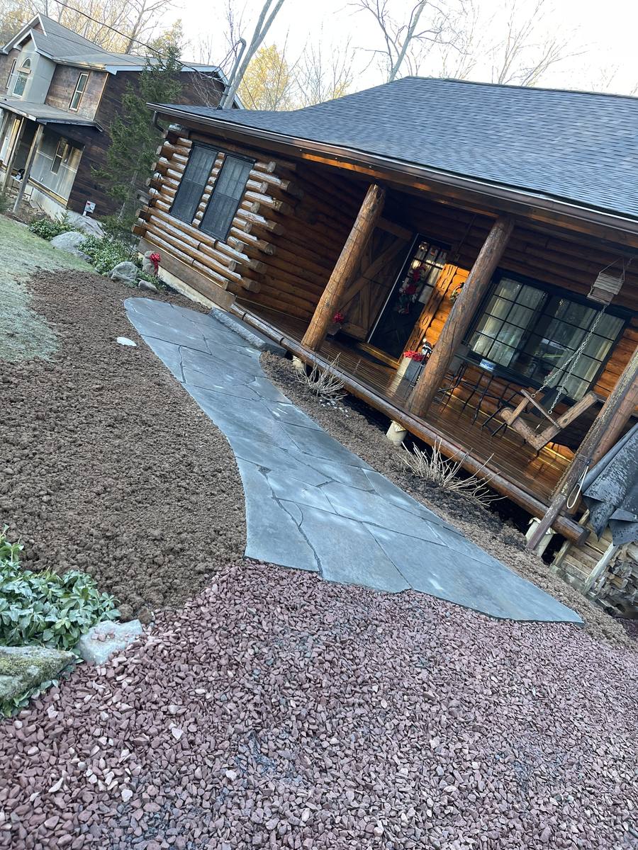 Curved flagstone walkway through fresh mulch beds leading to a log cabin's covered porch