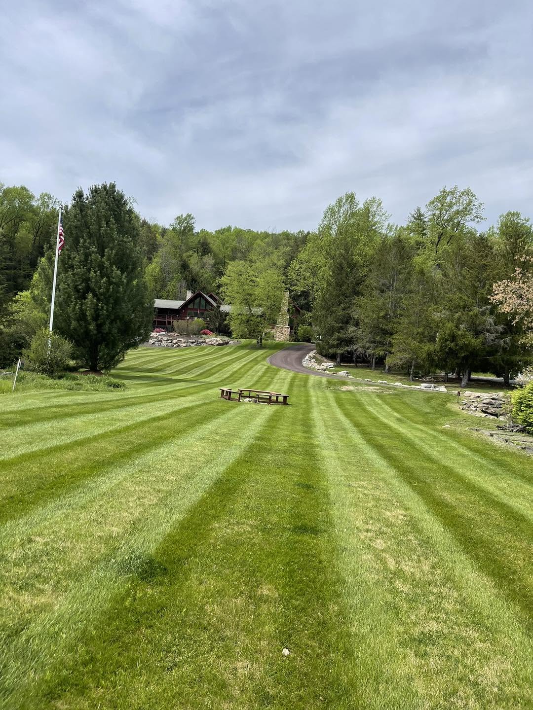 Wide striped lawn leading up to a log cabin-style home with a flagpole and picnic area